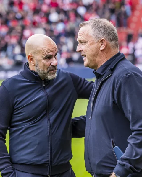 Peter Bosz en John van den Brom praten langs de zijlijn op een voetbalveld.