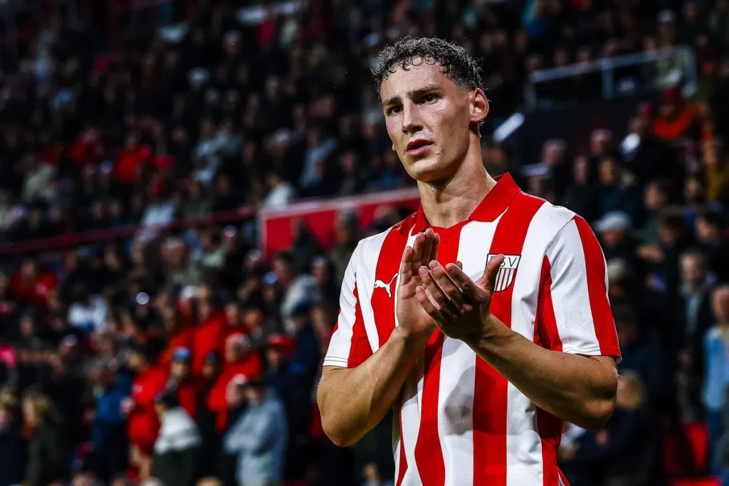 Voetballer in rood-wit gestreept shirt applaudisseert in een stadion.