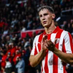 Voetballer in rood-wit gestreept shirt applaudisseert in een stadion.