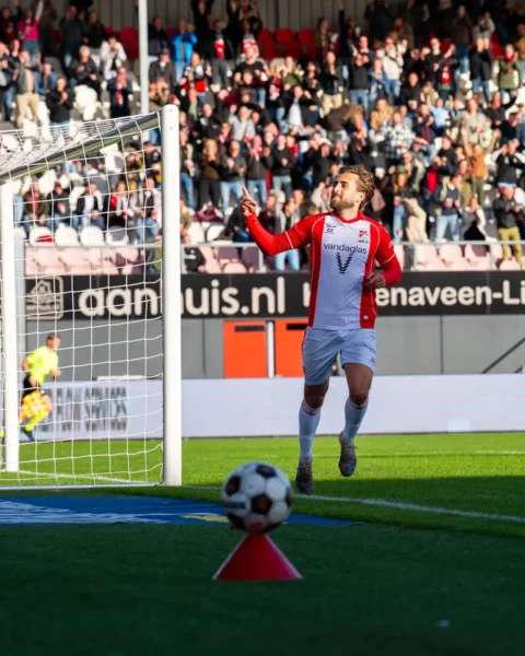 Voetballer van FC Emmen juicht naast het doel terwijl de doelman van Almere City toekijkt.