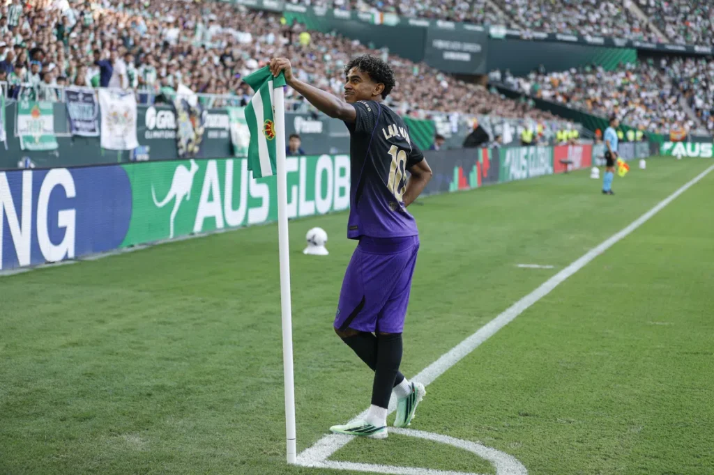 Lamine Yamal staat bij de hoekvlag in een stadion, met een groen-witte vlag in zijn hand.