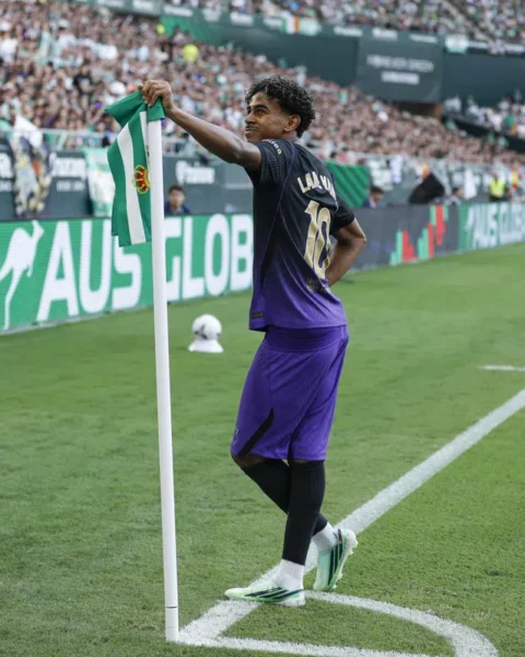 Lamine Yamal staat bij de hoekvlag in een stadion, met een groen-witte vlag in zijn hand.