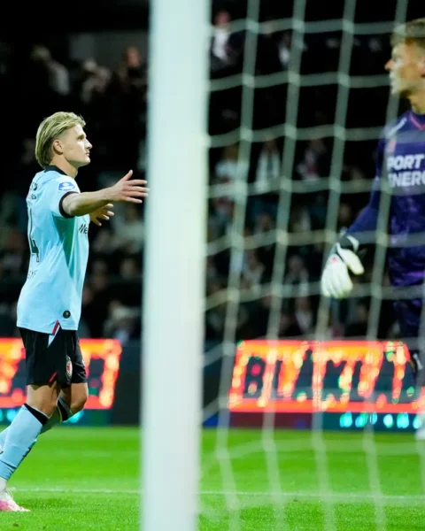 Sem Steijn in lichtblauw shirt juicht naast het doel tijdens een voetbalwedstrijd, met de keeper in paars op de achtergrond.