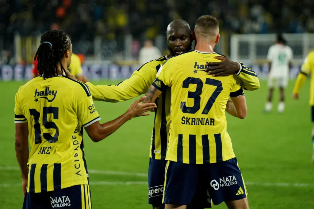Fenerbahçe-spelers in gele shirts staan elkaar op het veld vast na een moment in de wedstrijd.