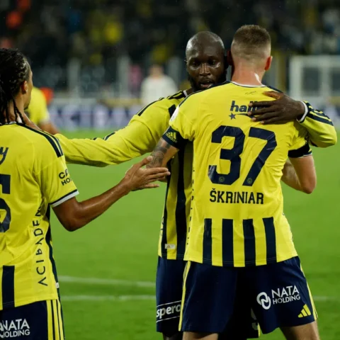 Fenerbahçe-spelers in gele shirts staan elkaar op het veld vast na een moment in de wedstrijd.