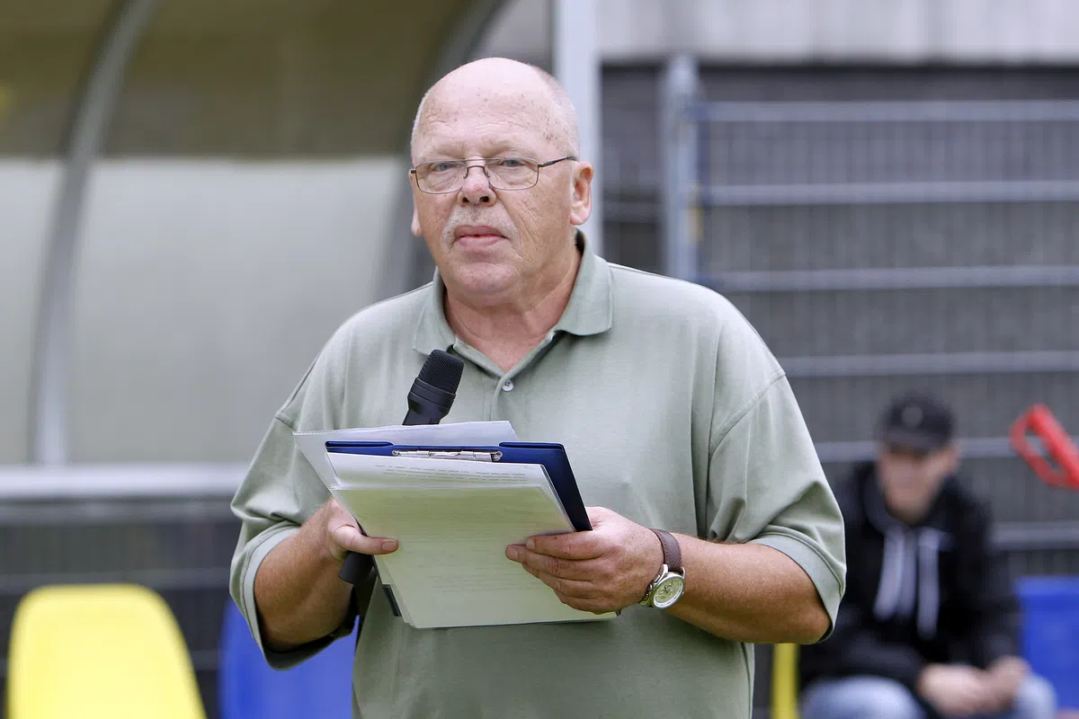 Een man met microfoon en klembord staat in een stadion.