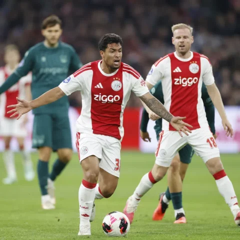 Ajax-spelers in actie tijdens een voetbalwedstrijd, met een speler in het rood-wit op de voorgrond bij de bal.