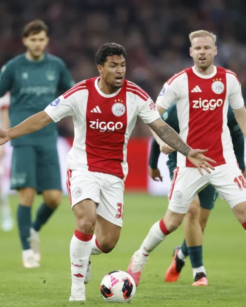 Ajax-spelers in actie tijdens een voetbalwedstrijd, met een speler in het rood-wit op de voorgrond bij de bal.