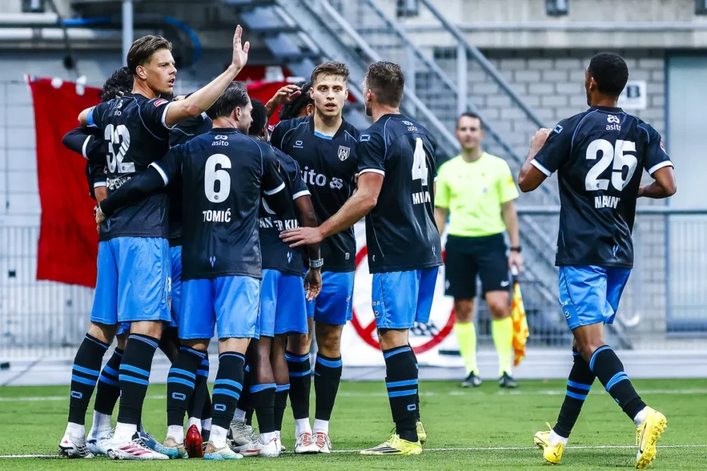 Voetballers in donkerblauwe shirts vieren een moment op het veld tijdens een wedstrijd.