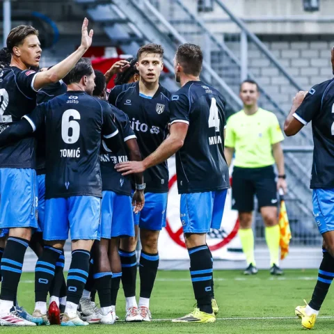Voetballers in donkerblauwe shirts vieren een moment op het veld tijdens een wedstrijd.