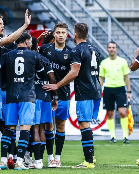 Voetballers in donkerblauwe shirts vieren een moment op het veld tijdens een wedstrijd.