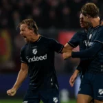 Twee FC Utrecht-spelers in donkerblauwe tenues vieren op het veld na een actie.