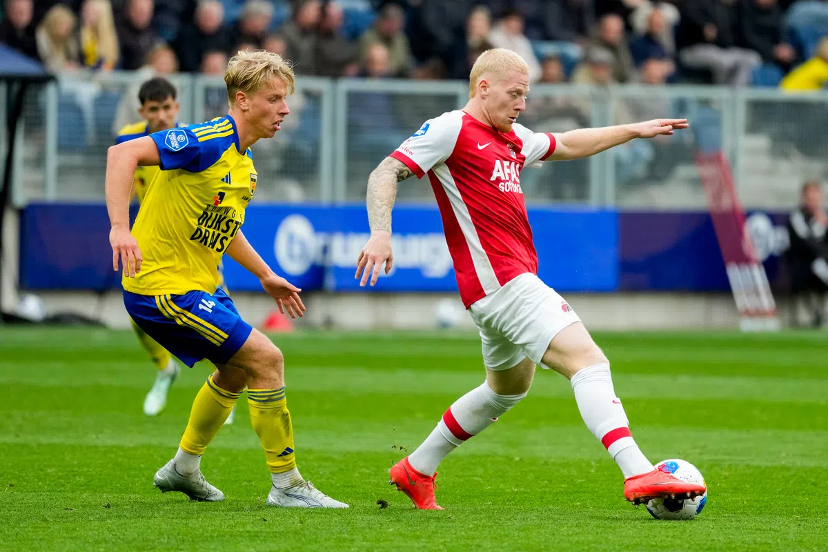 Twee voetballers in actie tijdens een wedstrijd, één in geel-blauw en één in rood-wit.
