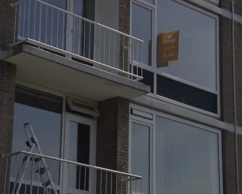 Appartementengebouw met een 'te koop'-bord achter een balkon.