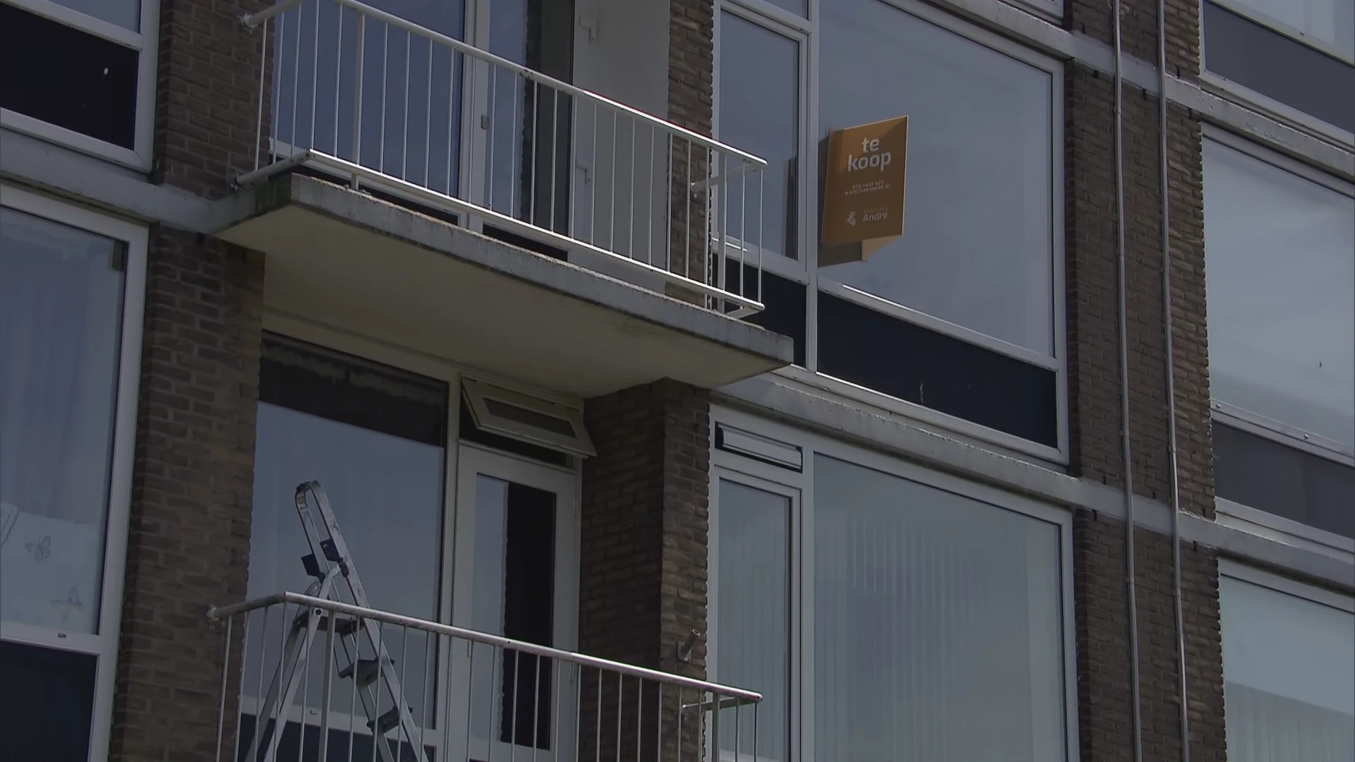 Appartementengebouw met een 'te koop'-bord achter een balkon.