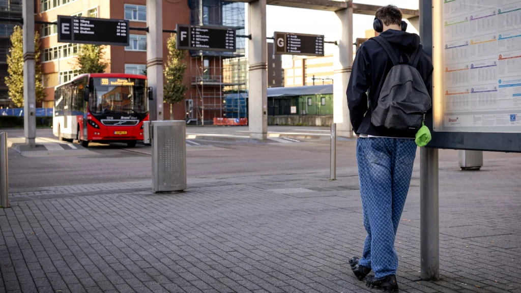 Een reiziger wacht bij een bushalte terwijl een bus op het station staat.