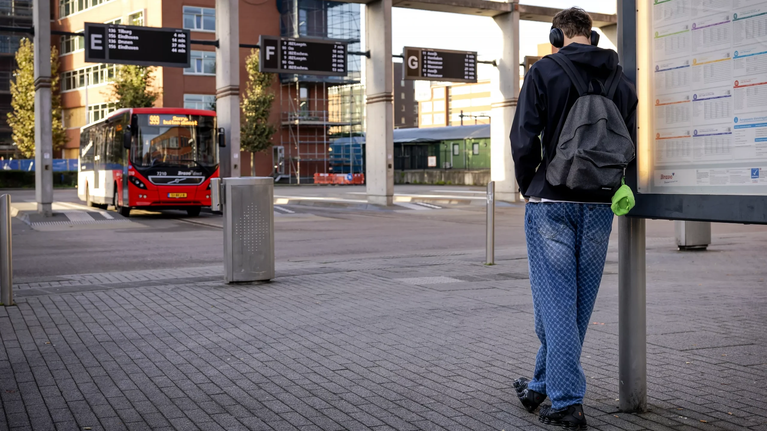 Een reiziger wacht bij een bushalte terwijl een bus op het station staat.