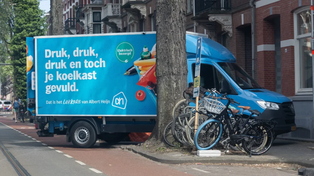 Albert Heijn-bezorgwagen geparkeerd in een straat met fietsen op de stoep.