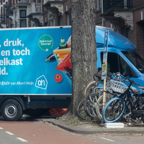 Albert Heijn-bezorgwagen geparkeerd in een straat met fietsen op de stoep.