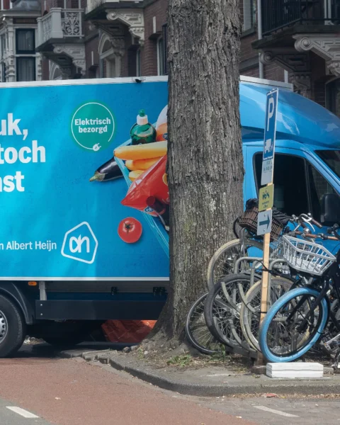 Albert Heijn-bezorgwagen geparkeerd in een straat met fietsen op de stoep.