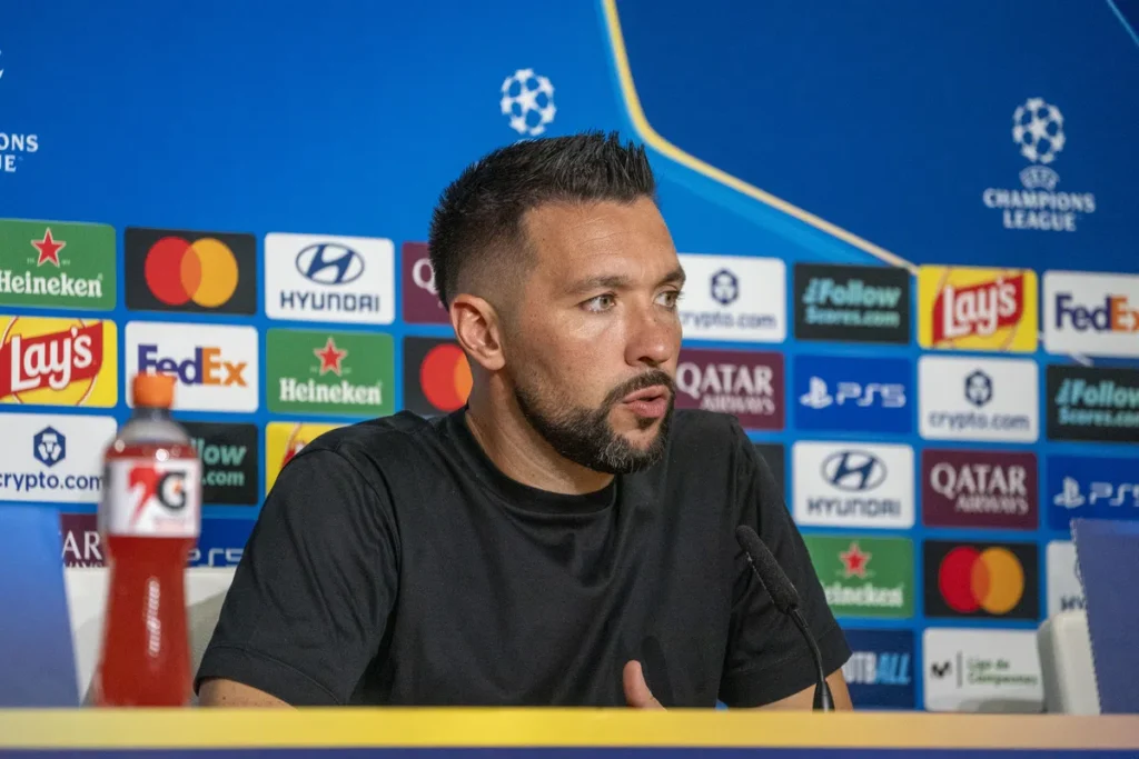 Francesco Farioli spreekt op een Champions League-persconferentie voor een sponsorachtergrond.