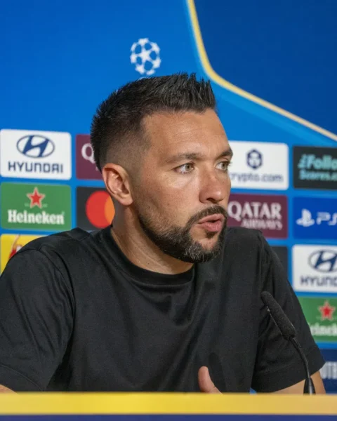 Francesco Farioli spreekt op een Champions League-persconferentie voor een sponsorachtergrond.
