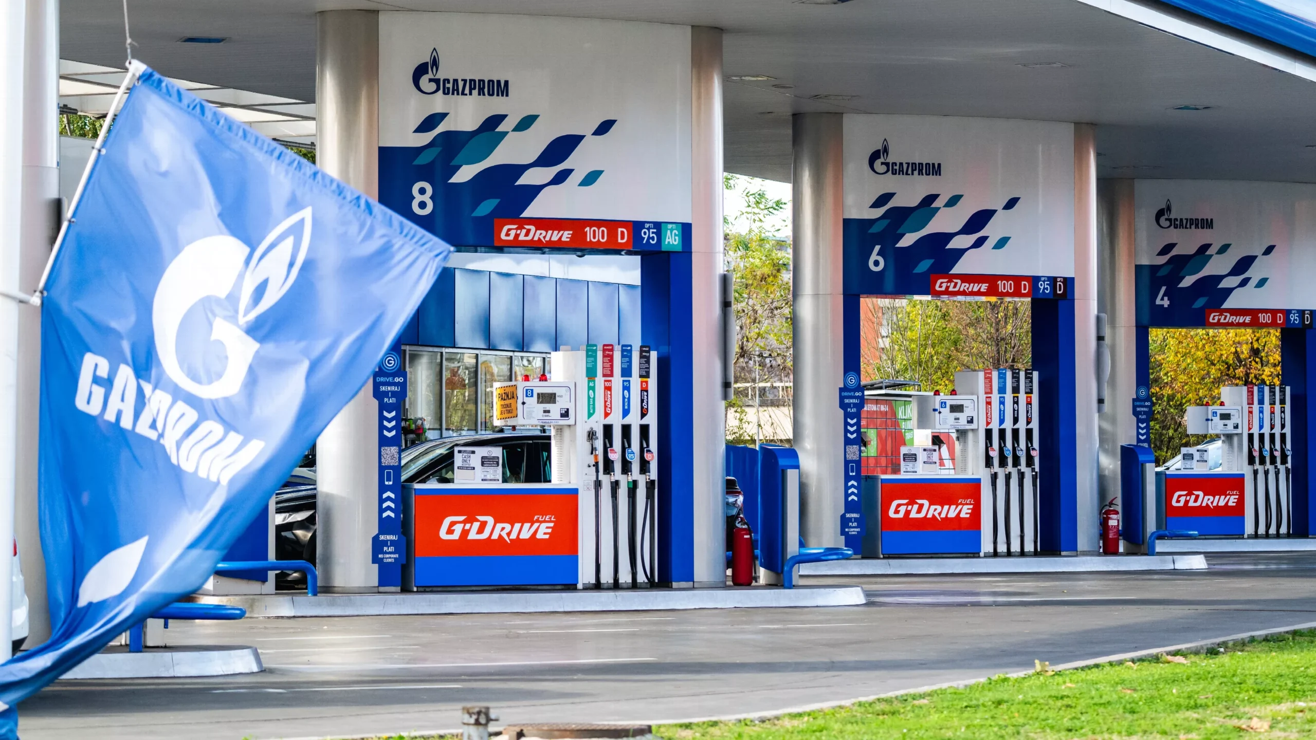 Gazprom-branded gas station pumps under a canopy, with a blue Gazprom flag in the foreground.