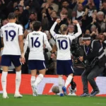 James Maddison viert een doelpunt voor Tottenham Hotspur, met teamgenoten naast hem en publiek op de achtergrond.
