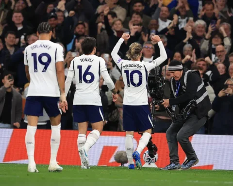 James Maddison viert een doelpunt voor Tottenham Hotspur, met teamgenoten naast hem en publiek op de achtergrond.