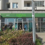 Een Żabka-winkelpui in een stedelijke straat met voorbijgangers ervoor.