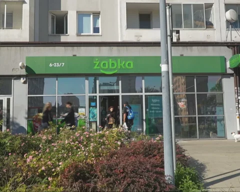 Een Żabka-winkelpui in een stedelijke straat met voorbijgangers ervoor.