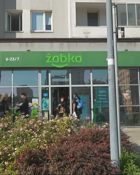Een Żabka-winkelpui in een stedelijke straat met voorbijgangers ervoor.