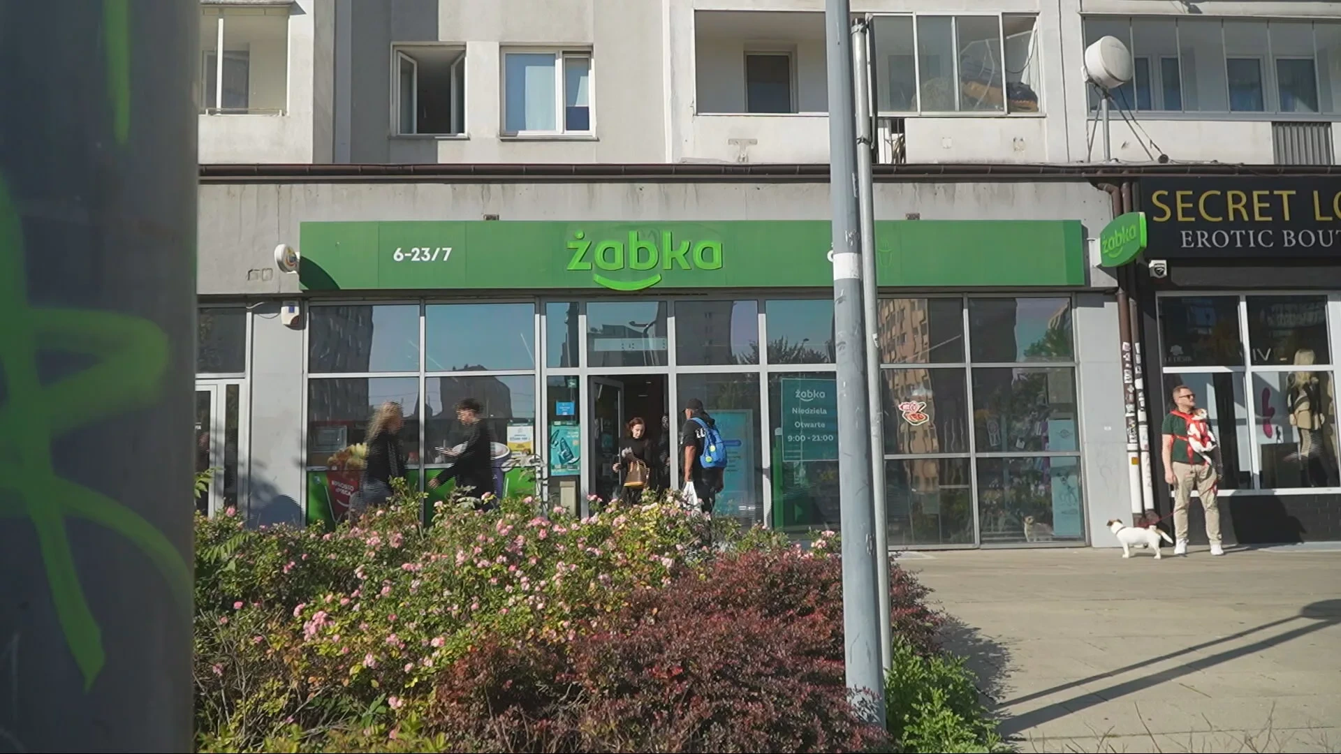 Een Żabka-winkelpui in een stedelijke straat met voorbijgangers ervoor.