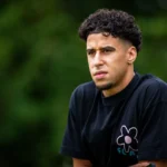Sami Ouaissa in een zwart T-shirt, buiten gefotografeerd tegen een groene achtergrond.