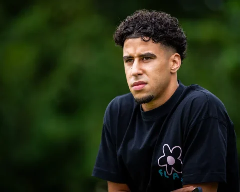 Sami Ouaissa in een zwart T-shirt, buiten gefotografeerd tegen een groene achtergrond.
