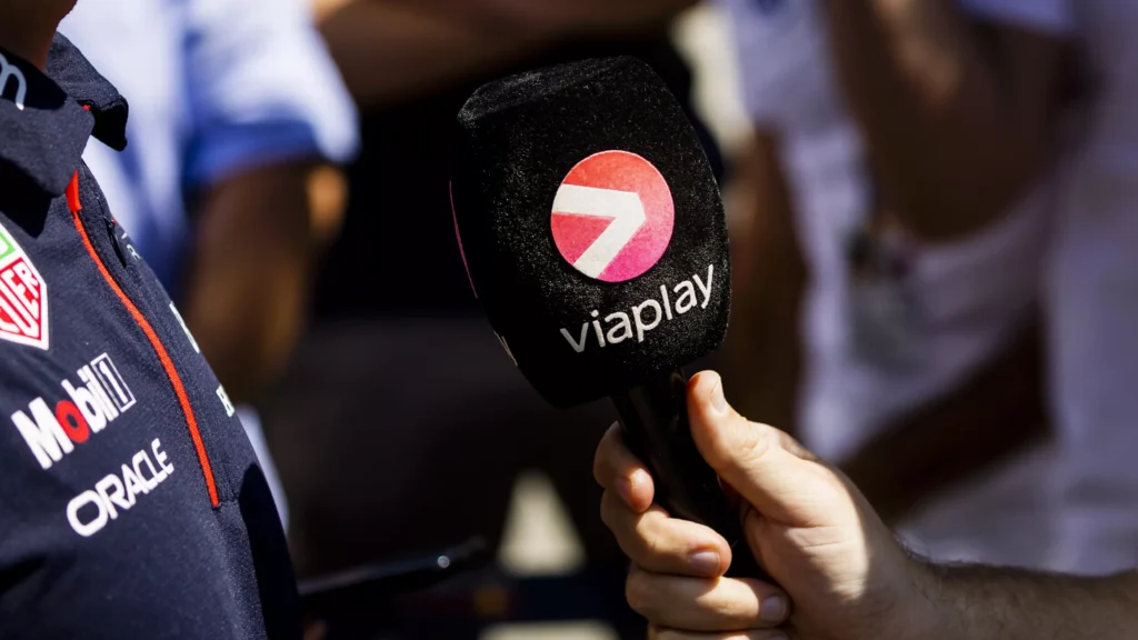 Een persoon houdt een microfoon met het Viaplay-logo vast naast een coureur in een raceteamshirt.