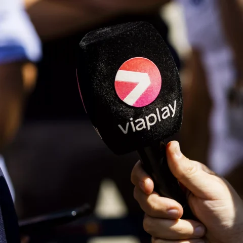 Een persoon houdt een microfoon met het Viaplay-logo vast naast een coureur in een raceteamshirt.