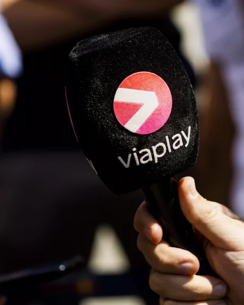 Een persoon houdt een microfoon met het Viaplay-logo vast naast een coureur in een raceteamshirt.