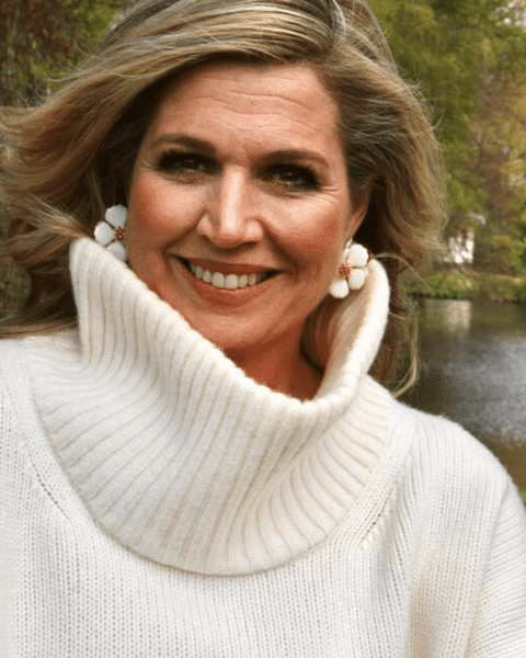 Portret van koningin Máxima in een witte coltrui bij een vijver in een park.