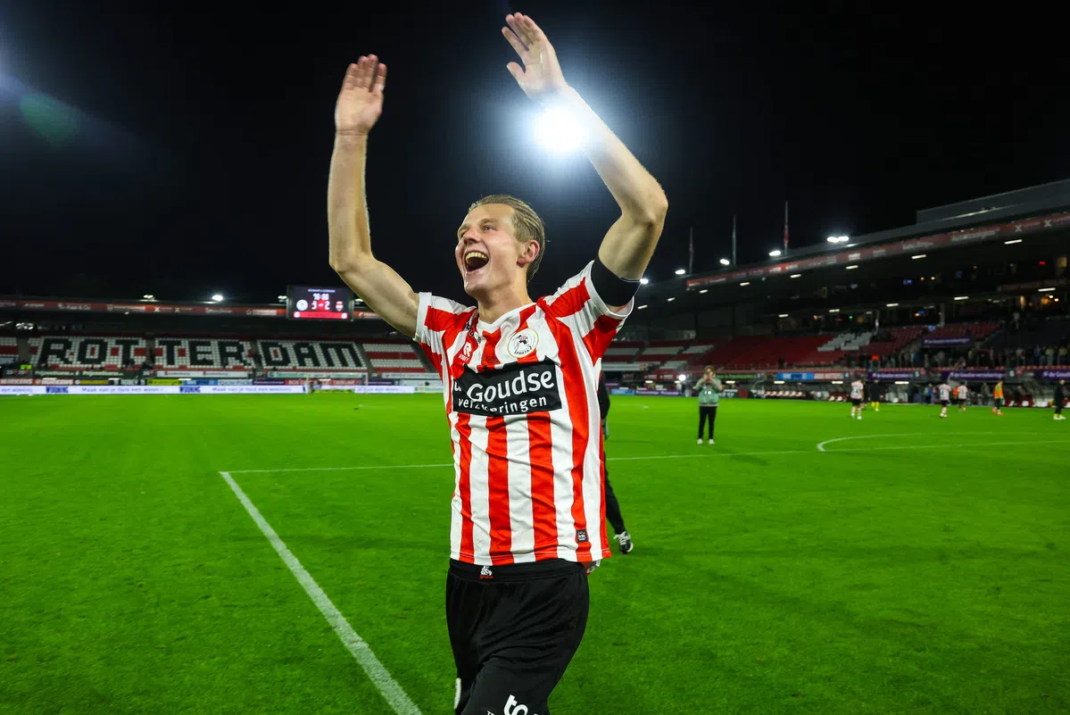 Een voetballer in rood-wit gestreept shirt juicht met beide armen omhoog op het veld.