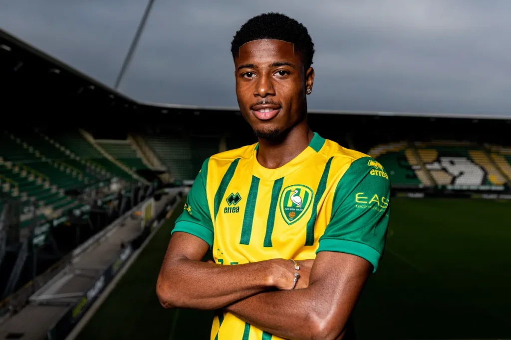 Een voetballer in een geel-groen ADO Den Haag-shirt poseert in een stadion.