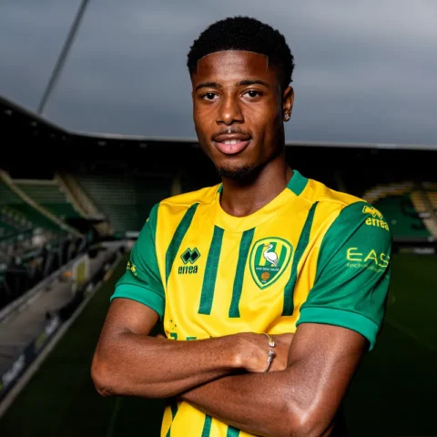 Een voetballer in een geel-groen ADO Den Haag-shirt poseert in een stadion.