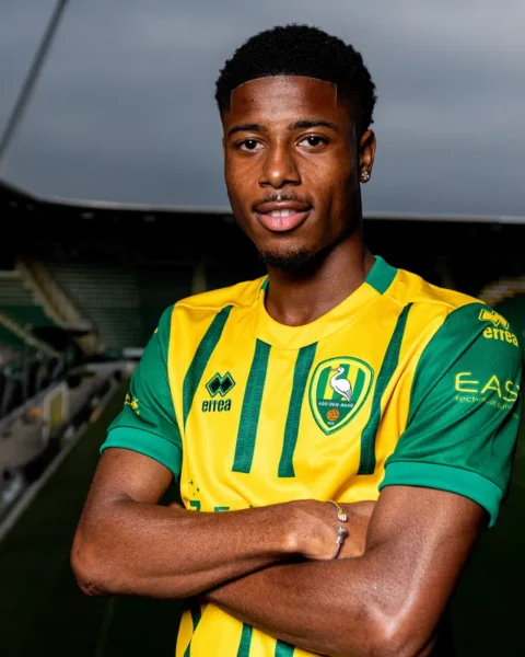 Een voetballer in een geel-groen ADO Den Haag-shirt poseert in een stadion.