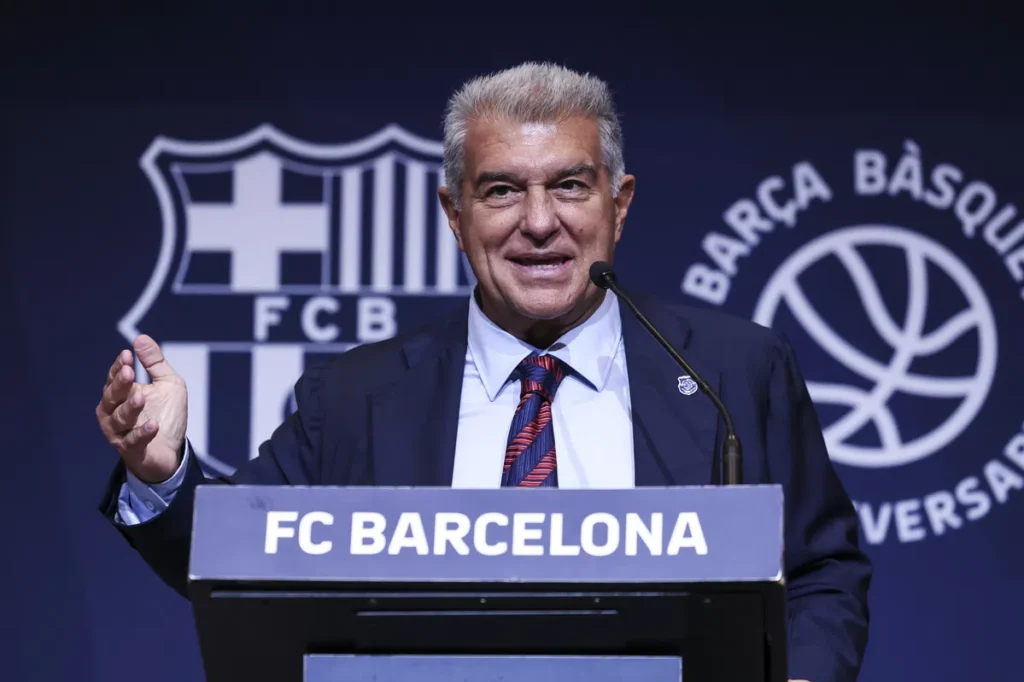 Joan Laporta spreekt bij een FC Barcelona-podium voor een blauw clubachtergrondscherm.