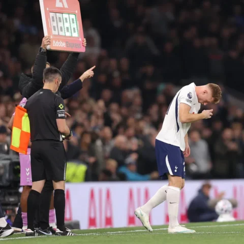 Tottenham-speler staat gebogen op het veld terwijl een bordwissel en officials naast hem staan.