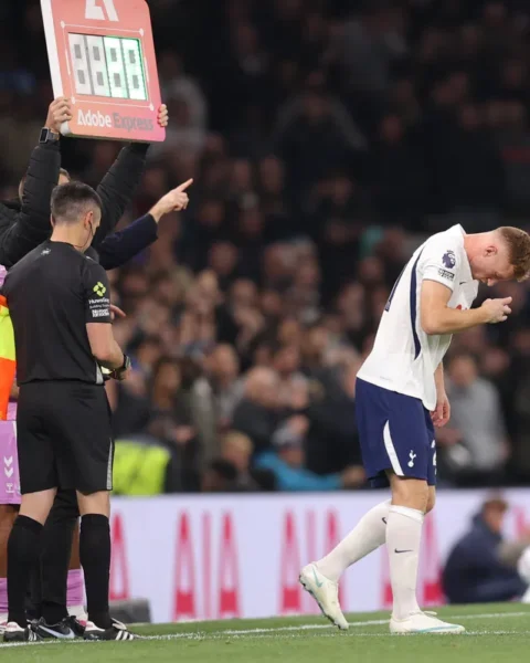 Tottenham-speler staat gebogen op het veld terwijl een bordwissel en officials naast hem staan.