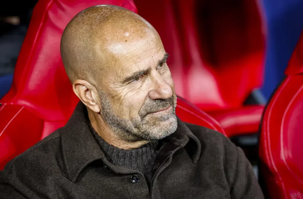 Peter Bosz zit op de bank in een rood stadionstoeltje.