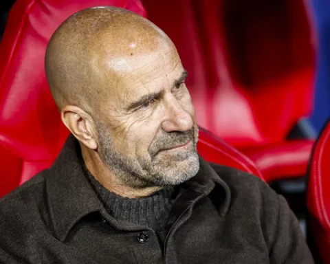 Peter Bosz zit op de bank in een rood stadionstoeltje.