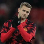 Matthijs de Ligt in een rood-zwarte Manchester United warming-upshirt, klappend op het veld.