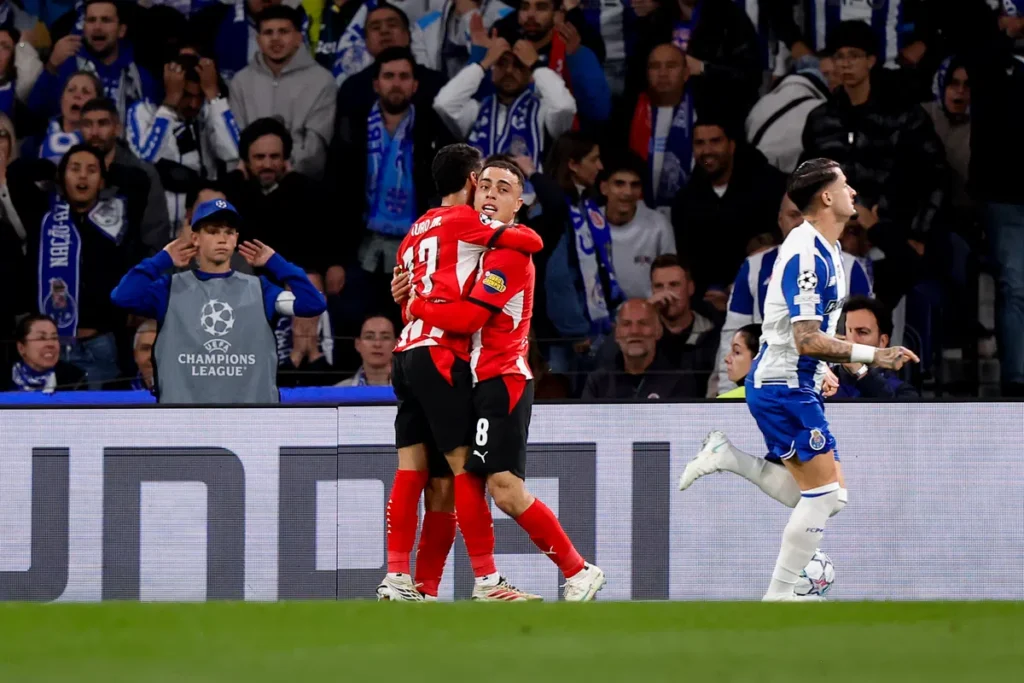 Sergiño Dest in een PSV-shirt loopt weg terwijl twee FC Porto-spelers elkaar omhelzen tijdens een Champions League-wedstrijd.